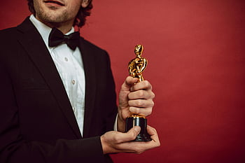 herec, cena, smoking, zlatá trofej, červené pozadí, úspěch, oslava, elegantní muž, socha oscara, hollywood, obřad