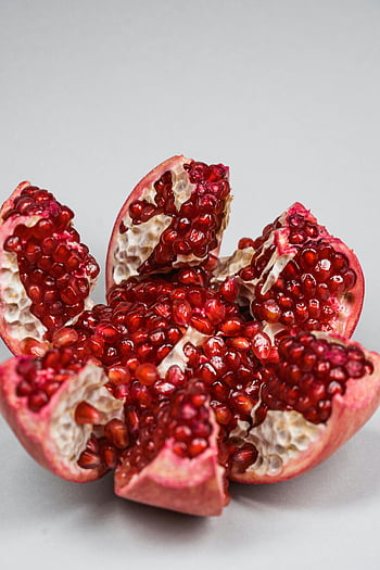 pomegranate, sliced pomegranate, vibrant red seeds, white surface, detailed view, fruit, pomegranate seeds, red seeds, close-up, healthy food, fresh fruit