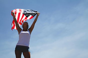 donna che ci tiene bandiera, festa dell'indipendenza, bandiera americana, chiaro cielo blu, giorno, Scena patriottica, Celebrazione all'aperto, bandiera USA, donna che celebra, momento festivo, orgoglio nazionale