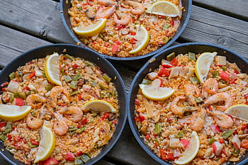 paella, seafood paella, lemon slices, wooden table, close-up, three pans, Spanish cuisine, rice dish, shrimp, mussels, vegetables
