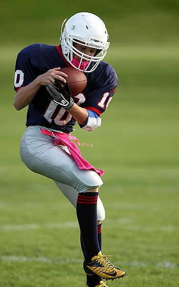 youth football player, catching pass, grassy field, athletic skill, selective-focus photography, football uniform, football helmet, sports action, outdoor game, youth sports, football glove