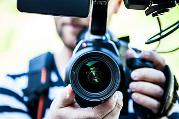 Canon DSLR camera, close-up photo, cameraman filming, camera lens, camera equipment, person holding camera, professional photography, video production, camera operator, outdoor filming, camera details