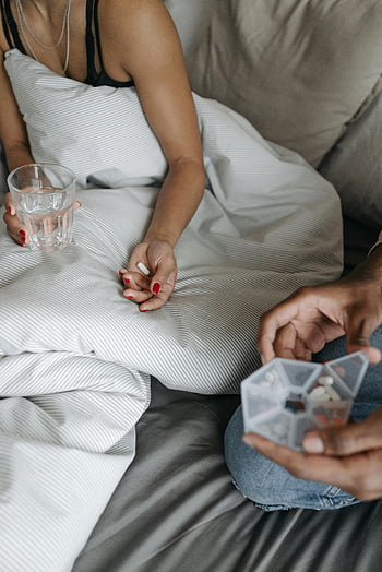 vrouw in bed, mouwloze top, glas water vasthouden, geneesmiddel, zorg tijdens ziekte, persoon in bed, gezondheidszorg, herstel, bedrust, pilorganisator, Comfortzorg