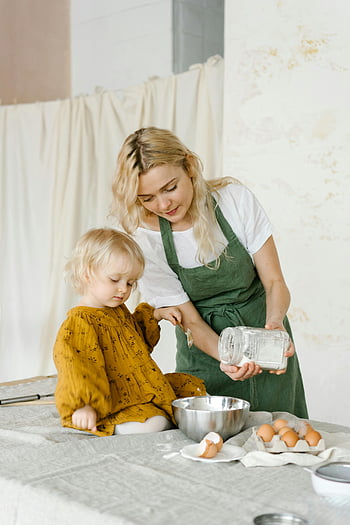 mother and daughter, baking together, bright kitchen, little cute girl, woman cooking, family activity, kitchen setting, baking ingredients, apron, eggs, mixing bowl