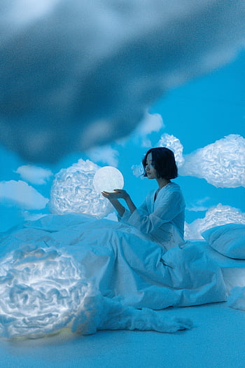 Asian woman, glowing orb, white bed, surreal clouds, serene night, cloud-filled room, dreamy atmosphere, soft lighting, peaceful scene, artistic composition, ethereal setting