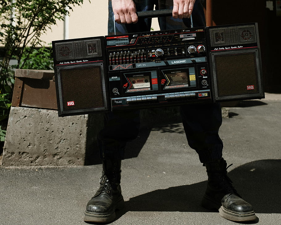 leather boots, black and red radio, vintage boombox, outdoor sunny day, person holding radio, Lasonic boombox, outdoor setting, sunny weather, retro audio equipment, black boots, vintage audio