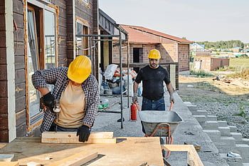 pracovníci na stavbě, Muž v černé košili, žlutá čepice, tlačit barrow, kolečko, stavba domu, pomocí pily, nesení materiálů, staveniště, venkovní práce, Bezpečnostní vybavení
