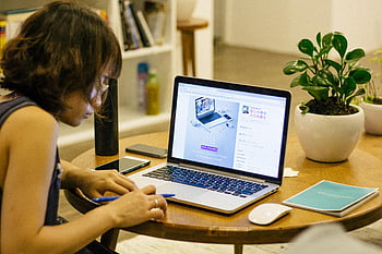 Frau, Schwarzes Panzerhemd, schwarzer Laptop, brauner Holztisch, Heimarbeit, digitaler Nomade, Innenministerium, Schreibtisch-Setup, Pflanze, Stift, Lebensstil