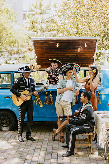 Mariachi Band, Venkovní oslava, vinobraní dodávka, živý výkon, mexická hudba, venkovní akce, Mariachi hudebníci, Slavnostní atmosféra, Kulturní oslava, modrá dodávka, řetězec světla