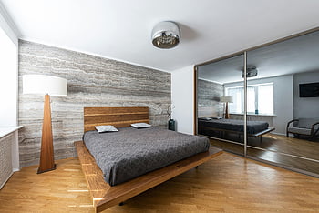 moderní ložnice, dřevěná postel, Velké zrcadlo, minimalistický dekor, přirozené osvětlení, Prostorný pokoj, stolní lampa, zrcadlová stěna, moderní design, dřevěné podlahy, Vzhled interiéru