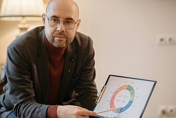 bald man, red sweater, business data, graph, office setting, man pointing, pencil, presentation, professional, data visualization, office environment