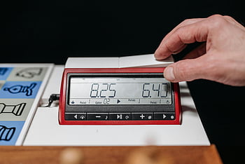 chess clock, digital chess clock, red chess clock, black chess clock, hand adjusting clock, chess game, close-up shot, chess timer, chess equipment, chess tournament, chess player