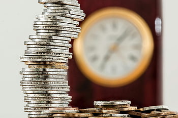 gestapelte Münzen, selektiver Fokus, verschwommene Uhr, Zeit und Geld, Nahaufnahme Bild, Münzenstapel, finanzielles Symbol, Geldbeziehung, Uhr Hintergrund, Münzturm, Selektive Fokusfotografie