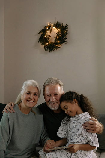 elderly couple, granddaughter, grandparents, festive wreath, family hug, holiday season, intergenerational bonding, warm embrace, home setting, cozy atmosphere, affectionate moment
