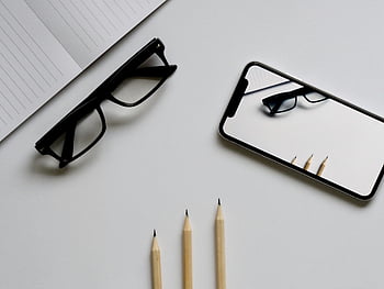 płaski układ, minimalistyczny, smartfon, okulary, ołówki, biały stół, odbicie, elegancki, białe tło, materiały biurowe, konfiguracja biurka