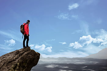 man standing on cliff, hiker in red jacket, scenic mountain view, bright blue sky, cliff edge, outdoor photography, adventure, nature, landscape, travel, backpacker