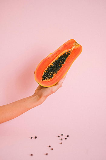 papaya, half papaya, fresh papaya, tropical fruit, pink backdrop, vibrant fruit, papaya seeds, hand holding papaya, tropical appeal, fruit photography, papaya half