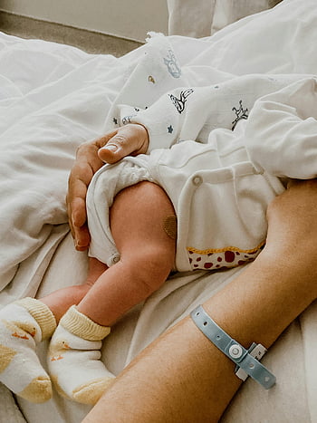 woman holding newborn, tender moment, mother and newborn, hospital setting, newborn baby, motherhood, baby care, hospital bed, newborn photography, baby socks, hospital bracelet