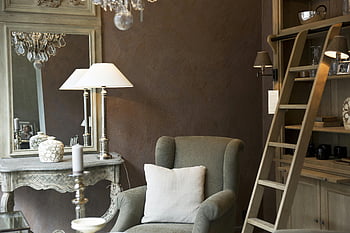 hnědý dřevěný žebřík, Šedé křeslo, elegantní interiér, vinobraní nábytek, dekorativní osvětlení, lustr, stolní lampa, bílý polštář, dřevěné police, ozdobené zrcadlo, svícen