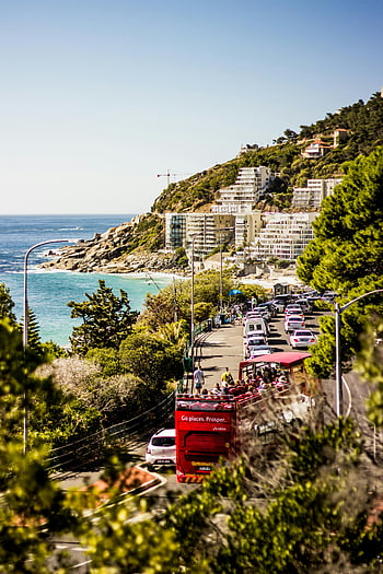 Cape Town, coastline, vibrant traffic, ocean views, blue sea, green mountains, cars on road, scenic drive, coastal road, tourist bus, cityscape