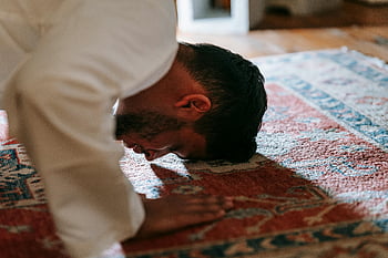 Muslim man, prayer ritual, traditional rug, white dress shirt, bowing down, indoor prayer, religious practice, Islamic prayer, prayer position, cultural ritual, spiritual practice