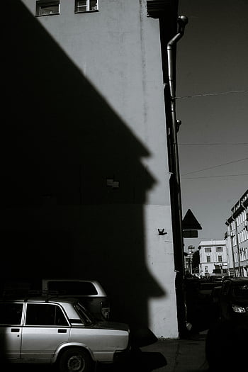 black and white, street scene, dramatic shadows, parked car, urban calmness, old car, tall building, town, monochrome photography, cityscape, architectural shadows