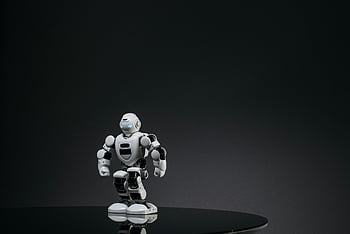 white robot toy, black surface, reflective surface, dark studio, modern technology, small robot, white robot, black background, toy robot, futuristic design, robot figure