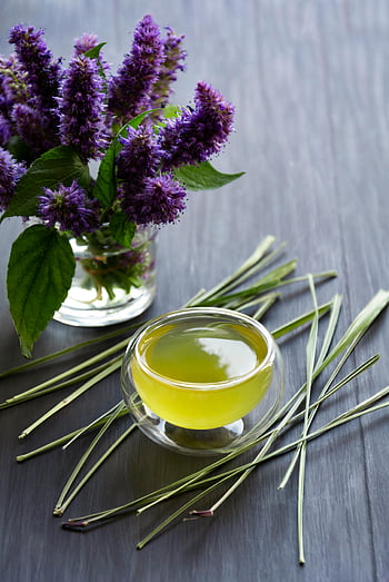 yrttitee, keltainen öljy, lasikuppi, sitruunaruoho, korealainen minttu, violetit kukat, liuskekivi tausta, virkistävä juoma, yrtti -infuusio, luonnollinen tee, aromaattiset yrtit