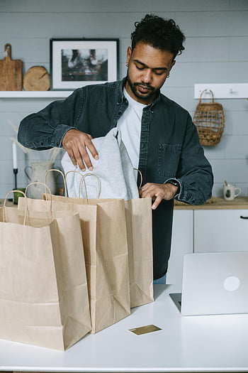 man, black suit jacket, white paper bag, organizing purchases, paper bags, laptop, modern home setting, adult man, kitchen counter, casual outfit, shopping