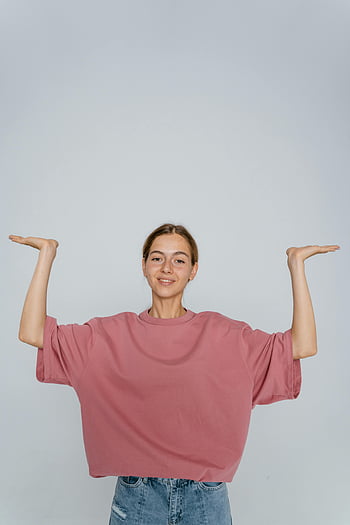 woman, pink t-shirt, jeans, raised arms, indoor pose, neutral background, casual outfit, studio photography, smiling woman, fashion portrait, lifestyle image