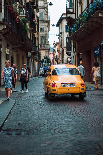 yellow sedan, cobblestone street, vintage car, Ferrazze Italy, pedestrians walking, charming scene, vintage yellow car, cobblestone road, people walking sidewalk, Italian street, European architecture