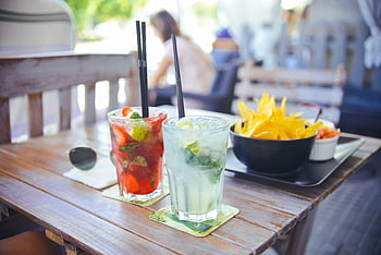 clear glass cups, brown wooden table, cocktails, straws, outdoor setting, sunglasses, snacks, mojito, fruit garnish, wooden bench, casual dining
