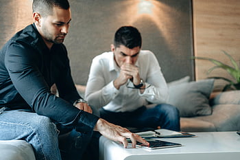 man in black shirt, touching device, cryptocurrency data, tablet analysis, serious discussion, indoor setting, two men, analyzing data, technology use, business meeting, casual attire