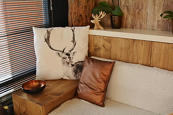 deer pillow, white and gray throw pillow, modern decor, rustic wooden elements, cozy living space, wooden shelf, indoor plants, brown leather pillow, wooden table, copper bowl, window blinds