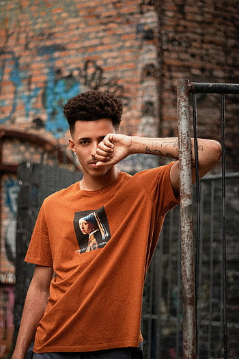 Vážný etnický muž, ošuntělý plot, městské pozadí, charismatický mladý muž, sebevědomá pozice, zvětralý plot, graffiti zeď, pouliční styl, Neformální outfit, městské módy, vytetovanou ruku