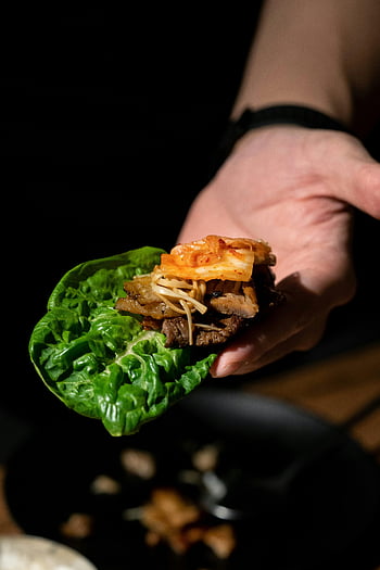Korean BBQ, lettuce wrap, kimchi, vibrant flavors, textures, hand holding, green leaf, meat, Korean cuisine, food photography, appetizing dish