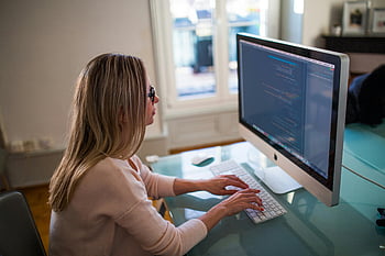 女性タイピング、 アップルマイティキーボード、 シルバーイマック、 ホームオフィス、 コーディング画面、 机のセットアップ、 屋内ワークスペース、 プロの環境、 コンピューター作業、 集中力のある個人、 テクノロジーの使用