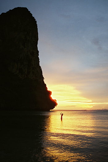 man in sea, cliff at sunset, Ao Nang Beach, dramatic silhouette, sunset scene, beach sunset, sea silhouette, cliff silhouette, person in water, sunset beach, dramatic sunset
