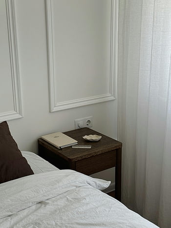 minimalist bedroom, white walls, brown nightstand, simple accessories, bedroom corner, nightstand near bed, white curtains, minimalist decor, bedroom furniture, simple bedroom, white bedding