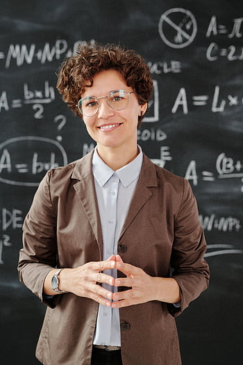 Žena v bundě hnědé obleky, brýle, učitel, Černá tabule, algebraické rovnice, sebevědomě se usmívá, třída, vzdělání, profesionální, sebejistý, učitel matematiky