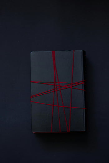 black book, red strings, top view, dark surface, copyspace, black cover, red thread, minimalist design, book binding, dark background, simple composition