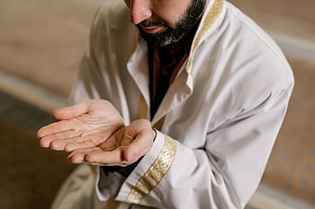 Muslim man, white thobe, kneeling, praying, mosque, cultural practices, religious practices, hands together, prayer gesture, Islamic attire, spiritual moment