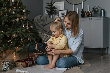 Boże Narodzenie, rodzina, matka i córka, otwieranie prezentów, zdobione drzewo, Święto w pomieszczeniach, sezon wakacyjny, żółty sweter, czarne pudełko upominkowe, Świąteczna atmosfera, Radosny moment
