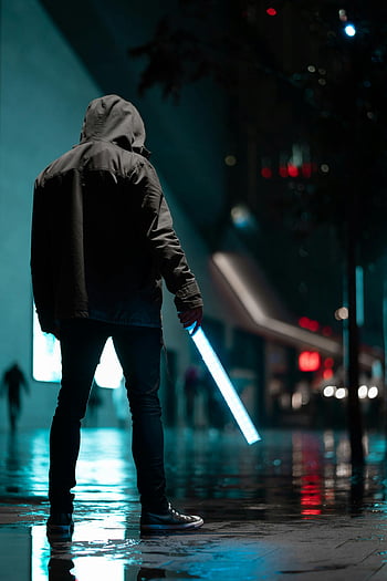 man in hoodie, night street, glowing light stick, rainy city, concrete pavement, urban night scene, silhouetted person, hooded figure, nighttime urban, light reflection, wet pavement