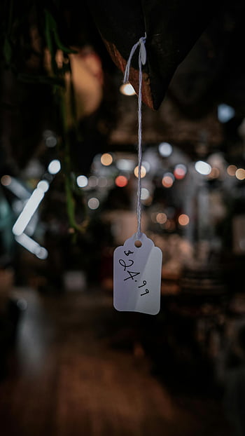 hanging price tag, artistic close-up, dimly lit, blurred setting, price tag, close-up photography, bokeh effect, indoor setting, product tag, string tag, price label