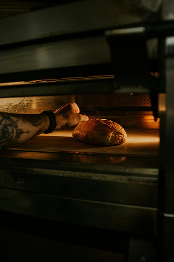 baker, tattooed arm, freshly baked bread, oven, artisanal craftsmanship, bread baking, bakery, bread removal, bread loaf, baking process, oven interior