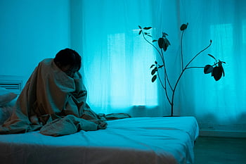 donna solitaria, seduto sul letto, avvolto nella coperta, solitudine, depressione, illuminazione blu, Scena indoor, figura solitaria, umore emotivo, Ambiente camera da letto, pianta in background