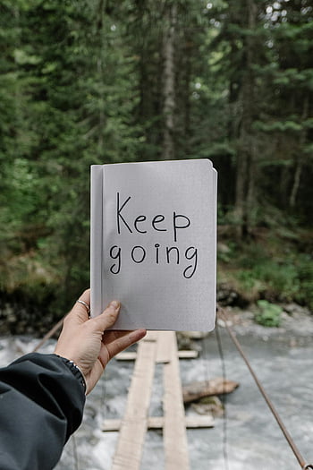 keep going, notebook, forest backdrop, river, nature motivation, hand holding, paper text, outdoor scene, motivational quote, natural setting, inspirational message