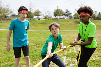 boys playing tug of war, grass, sunny park, colorful headbands, group of kids, outdoor activity, children playing, tug of war game, summer fun, park games, kids in park
