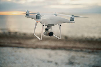 white quadcopter drone, seaside sunset, aerial views, flying drone, tranquil beach, sunset photography, drone photography, quadcopter, seaside aerial, sunset drone, white drone